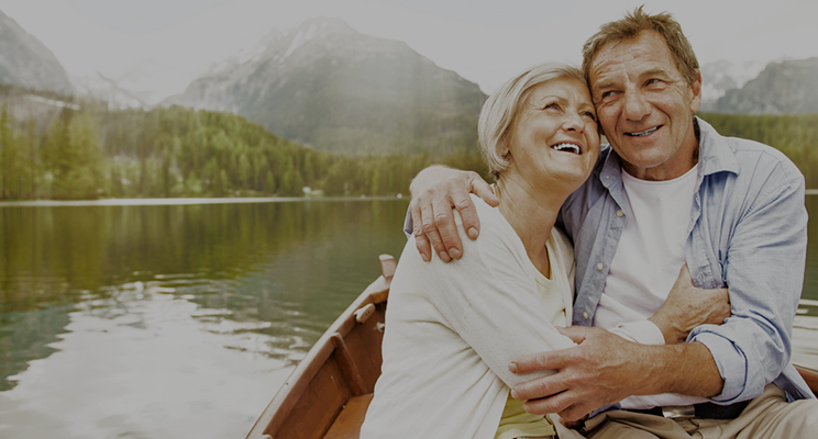 Smiling couple embracing in a boat on a lake with mountains in the background