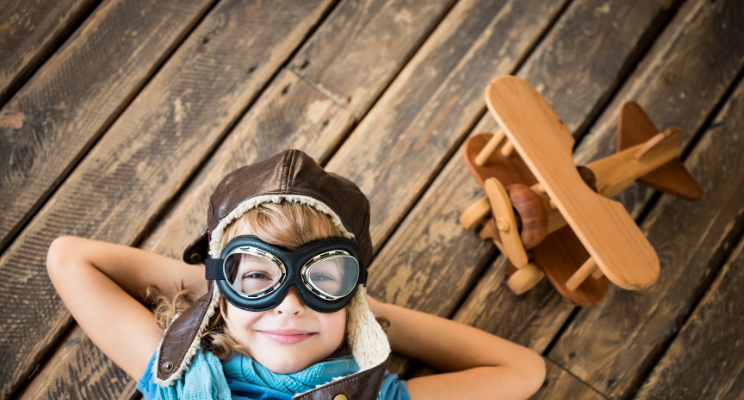 Child in aviator goggles with wooden airplane