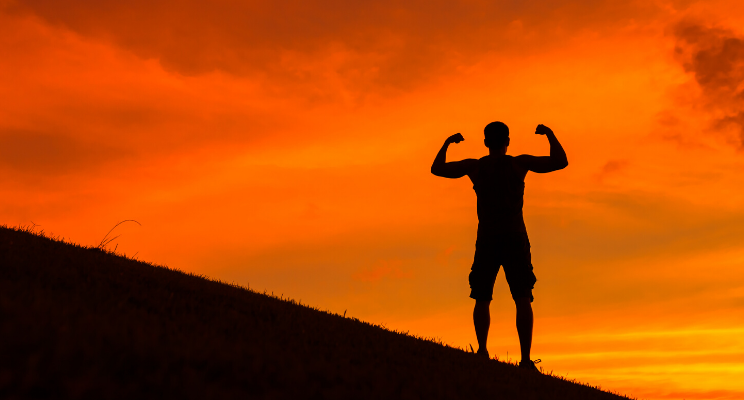Silhouette of person flexing at sunset