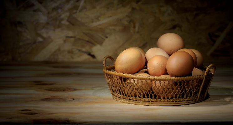 Wicker basket of brown eggs on wooden table