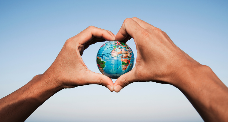 A person shaping their hands into a heart shape with an image of the world in the middle